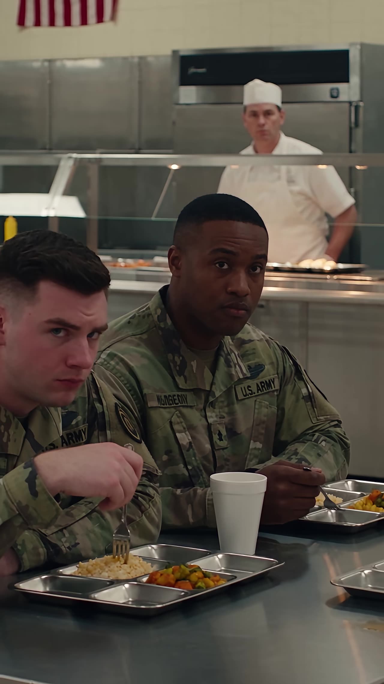 Two young soldiers staring in shock from mess hall table with trays