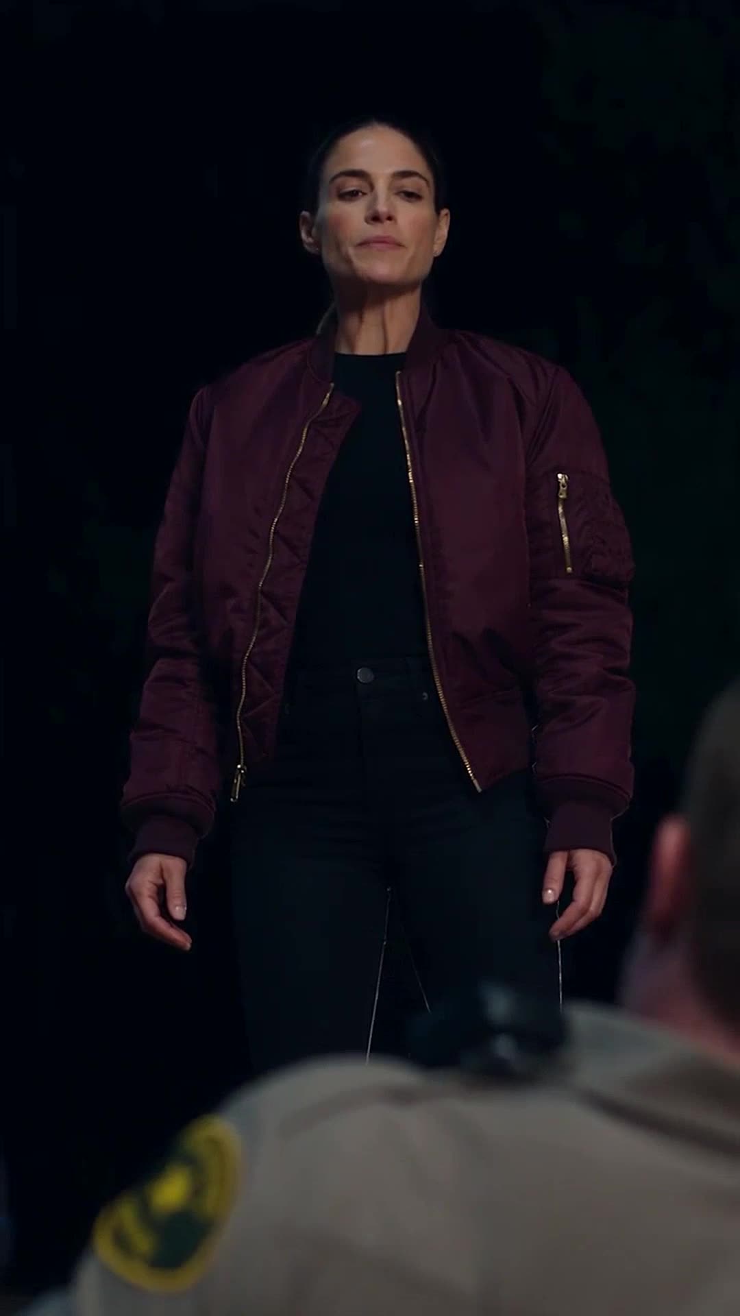 Undercover Commander Valérie Lawson stands calmly in her maroon jacket looking down at the fallen officer