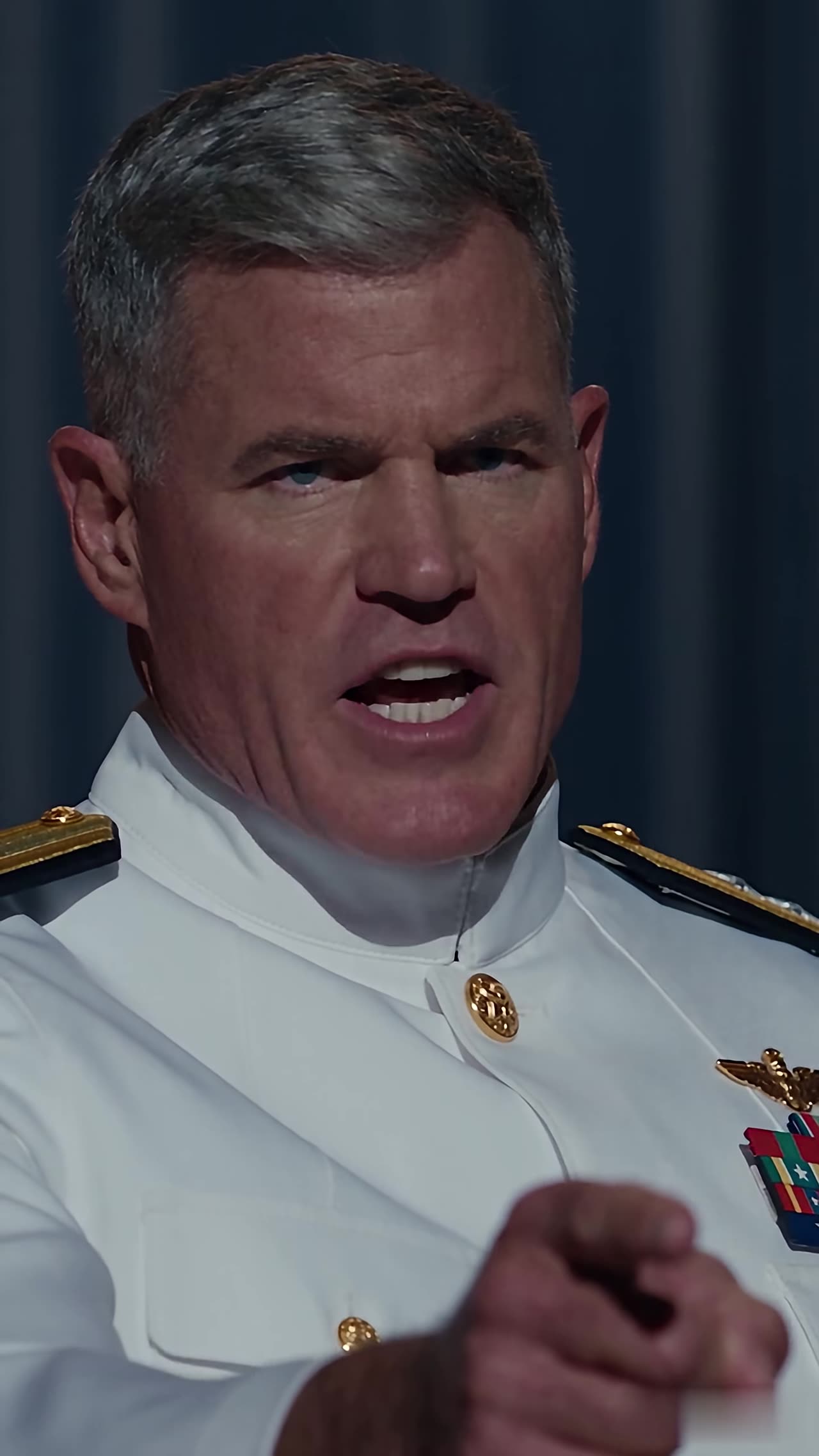 Admiral in white uniform points to call student onstage