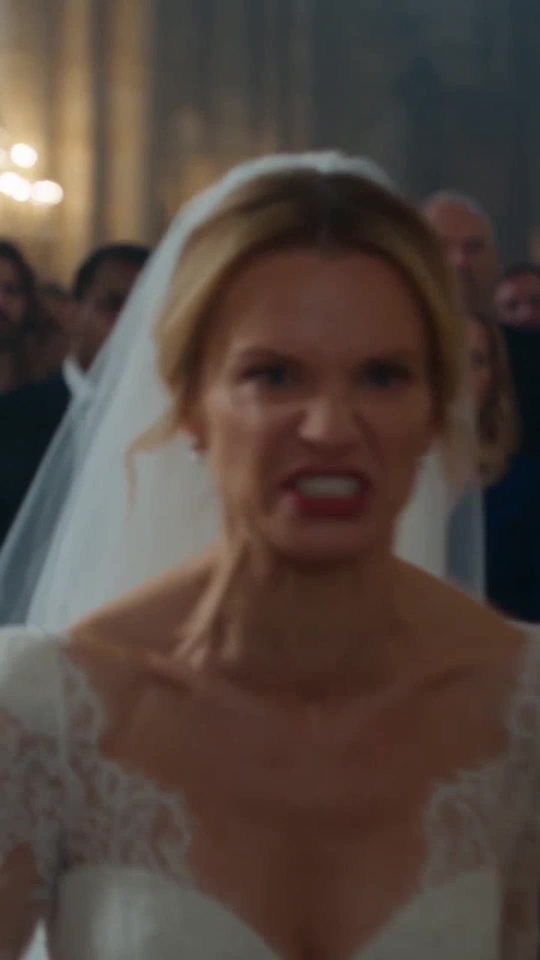 A furious bride in a white wedding gown scowls in rage toward the church aisle.