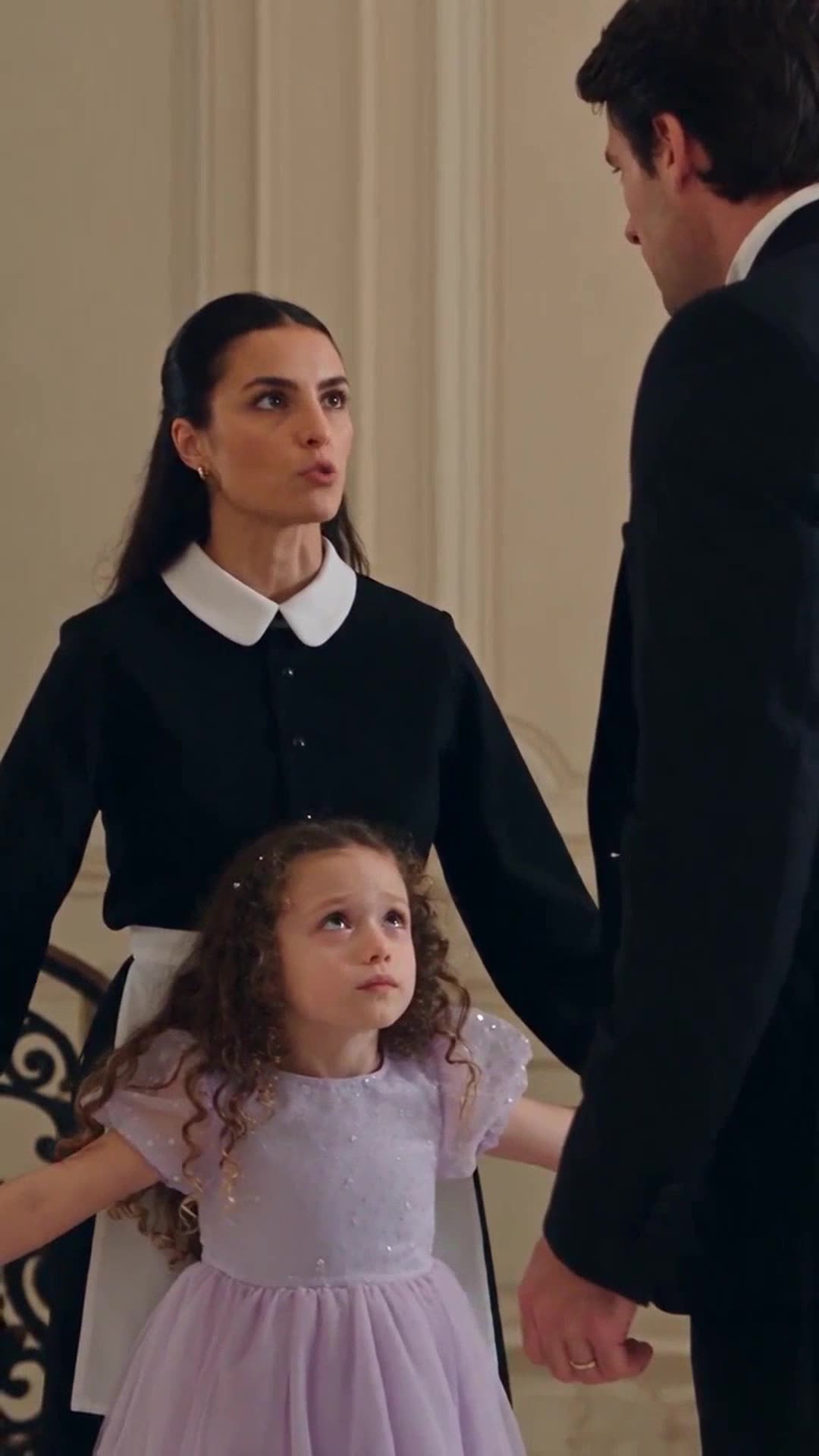 Émilie in her maid uniform stands protectively behind young Léa while speaking firmly to Julien Caldwell.