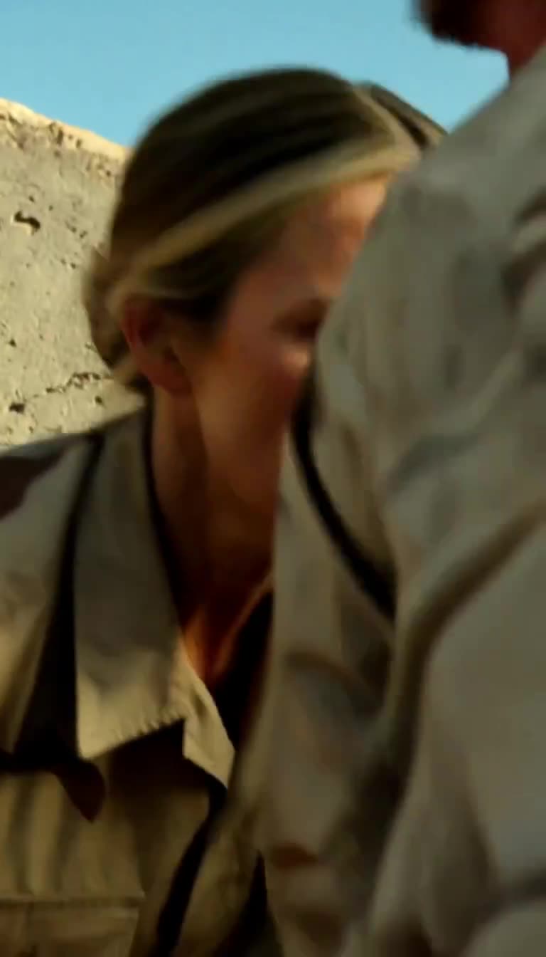 Blurry action shot of female officer ducking low next to sergeant behind a concrete wall under bright sky